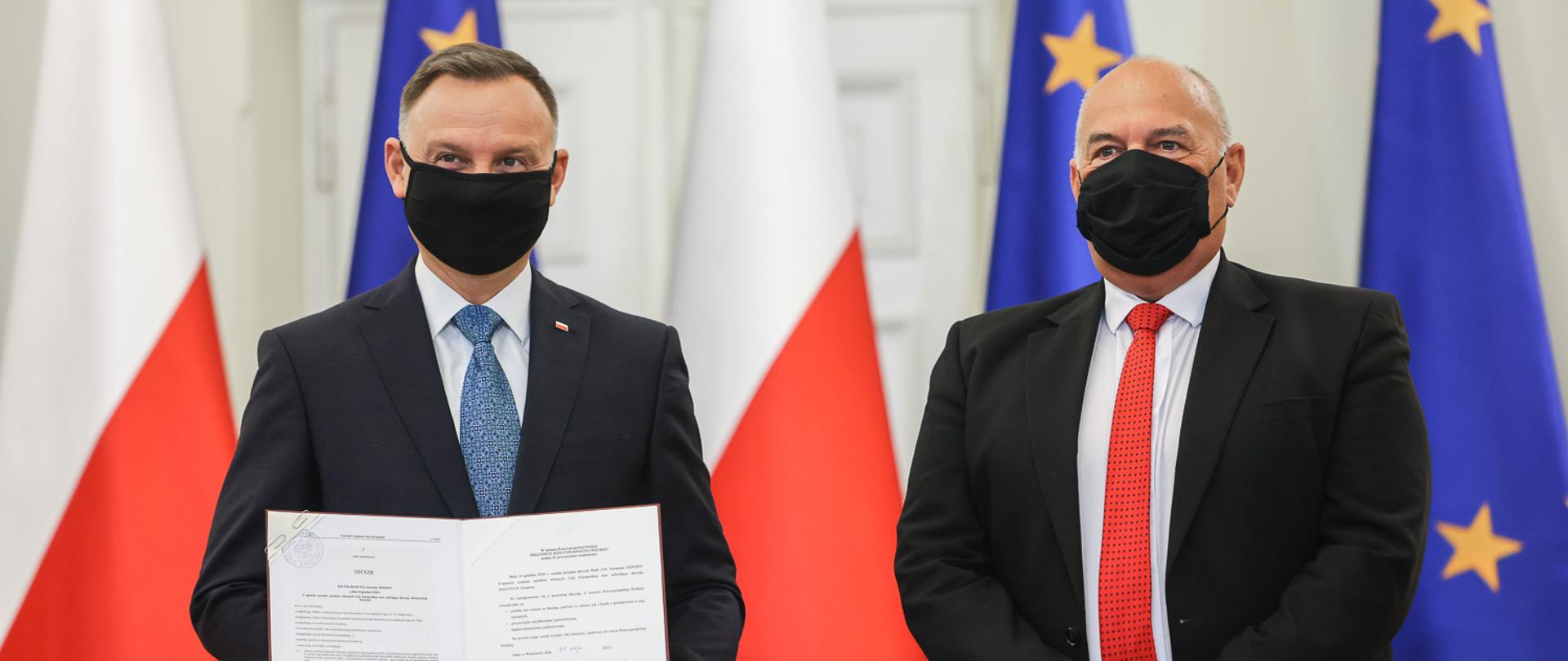 Prezydent Duda i Minister Kościński stoją z podpisaną ustawą, w tle stoją flaga Polska i UE 