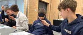 Uczniowie wypełniający arkusze oceny podczas warsztatów sensorycznych w KPODR Minikowo. Na stole widoczne papierowe kubki do degustacji soków i olejków.