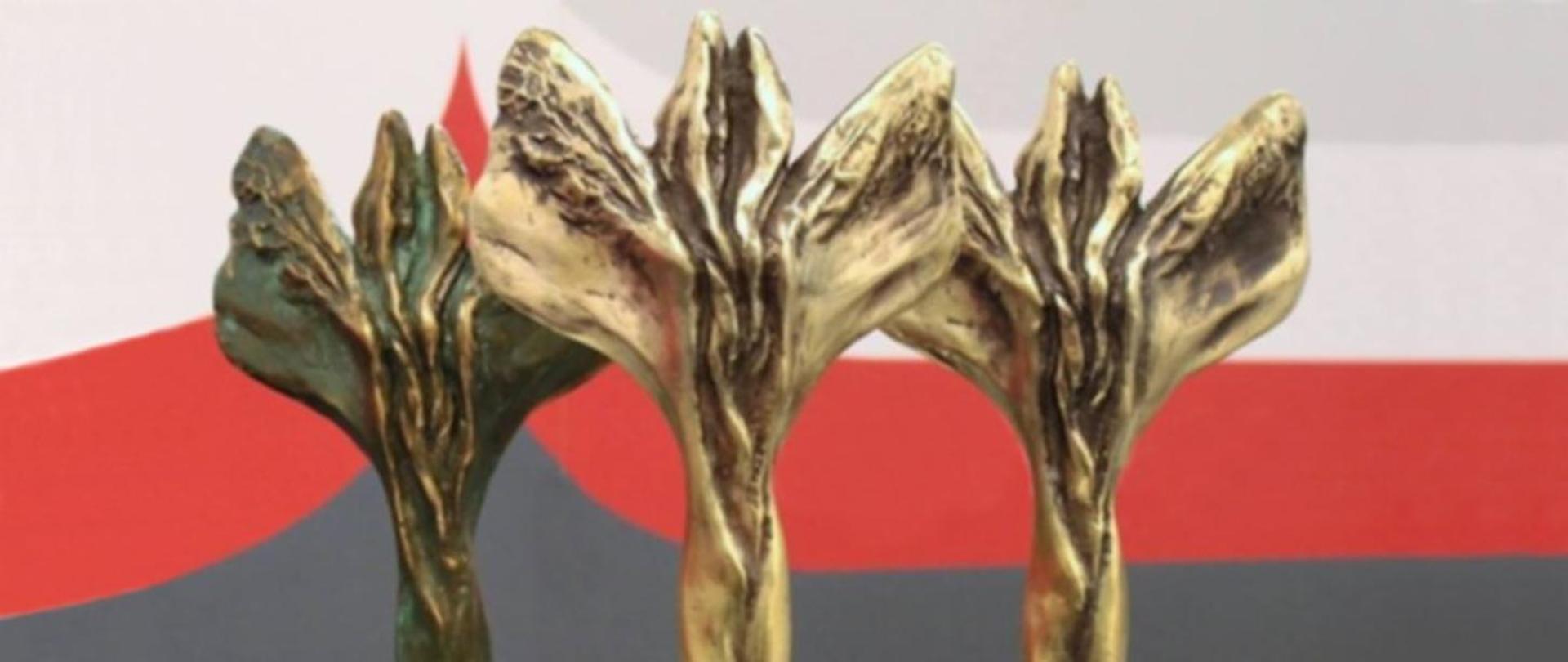 trzy statuetki na tle biało-czerwono-szarym tle