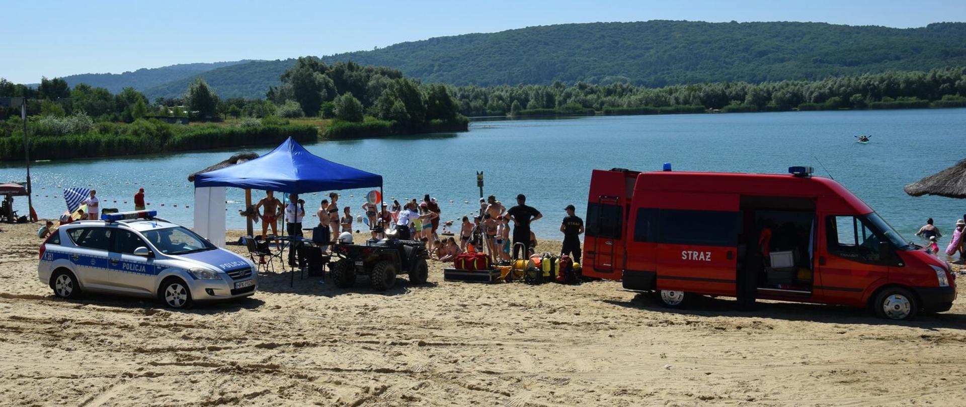 Na zdjęciu samochód policyjny i strażacki podczas prelekcji dla dzieci na plaży