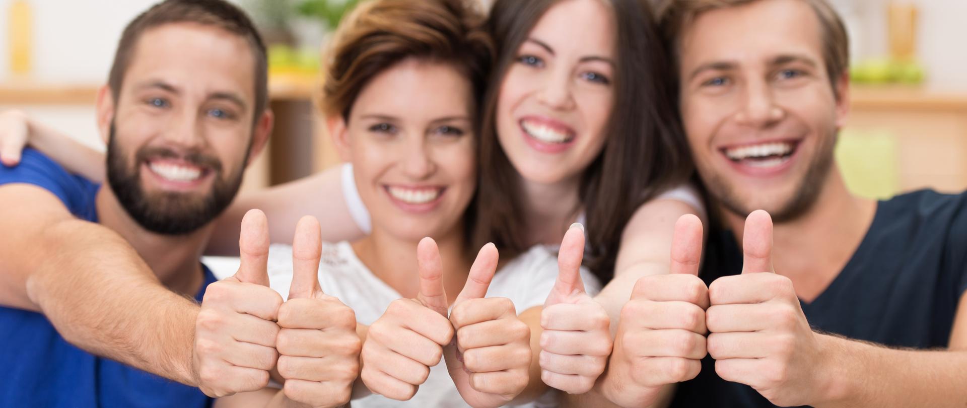 Młodzi uśmiechnięci ludzie z podniesionymi kciukami do góry