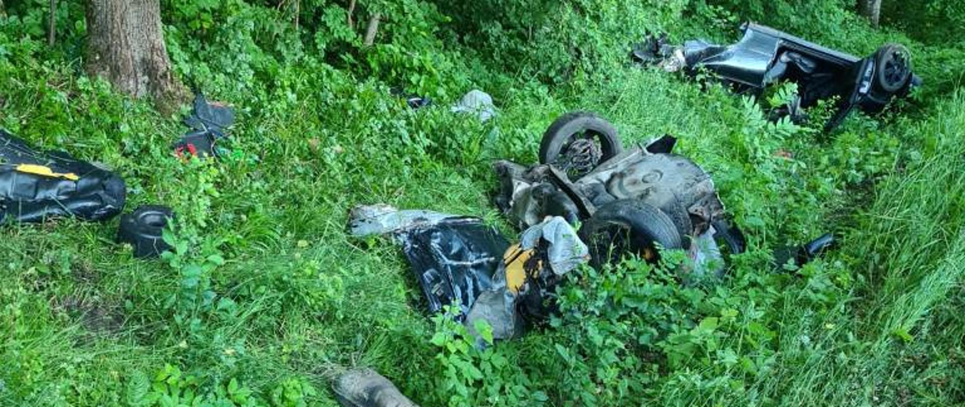 Na poboczu leży rozerwany na części samochód osobowy, po zderzeniu z drzewem.