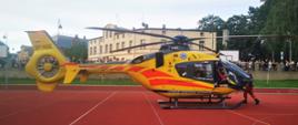 Zdjęcie przedstawia żółty śmigłowiec LPR, który wylądował na boisku szkolnym.