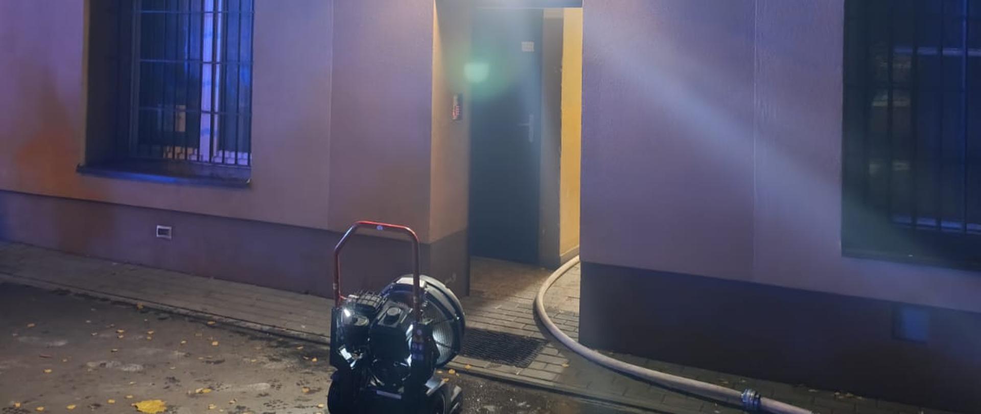 Na zdjęciu widoczny budynek w którym doszło do pożaru mieszkania. W drzwiach wejściowych widoczny wentylator oddymiający. 