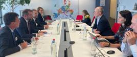 Minister funduszy i polityki regionalnej Grzegorz Puda i Dyrektor Generalny DG REGIO w Komisji Europejskiej Normunds Popens siedzą przy stole na przeciw siebie, obok nich siedzą pozostali uczestnicy spotkania