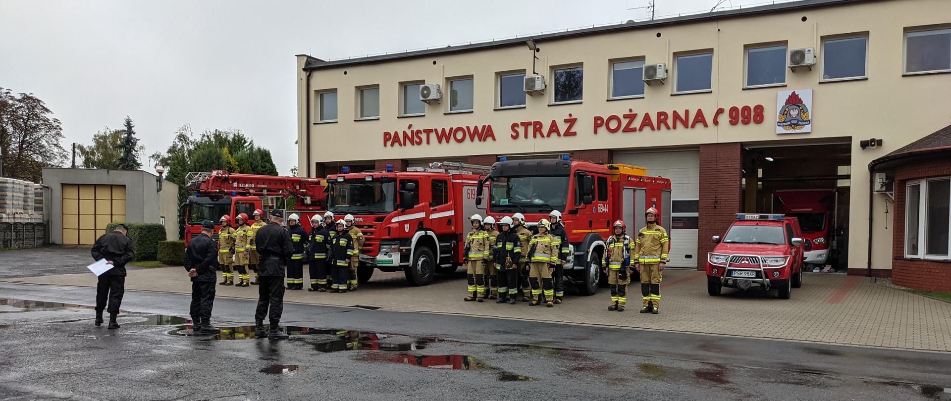 Zbiórka strażaków podczas inspekcji gotowości bojowej. Strażacy stoją na tle pojazdów pożarniczych na terenie KP PSP Środa Wlkp.
