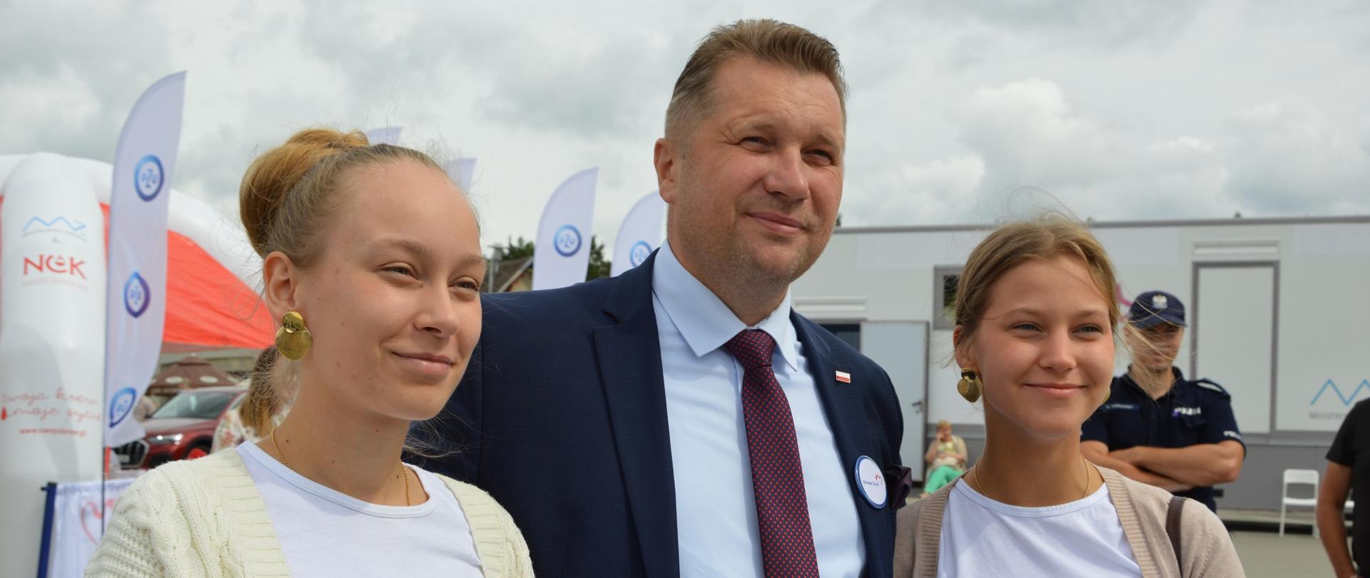 Minister Czarnek stoi obok dwóch młodych kobiet.