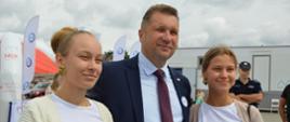 Minister Czarnek stoi obok dwóch młodych kobiet.