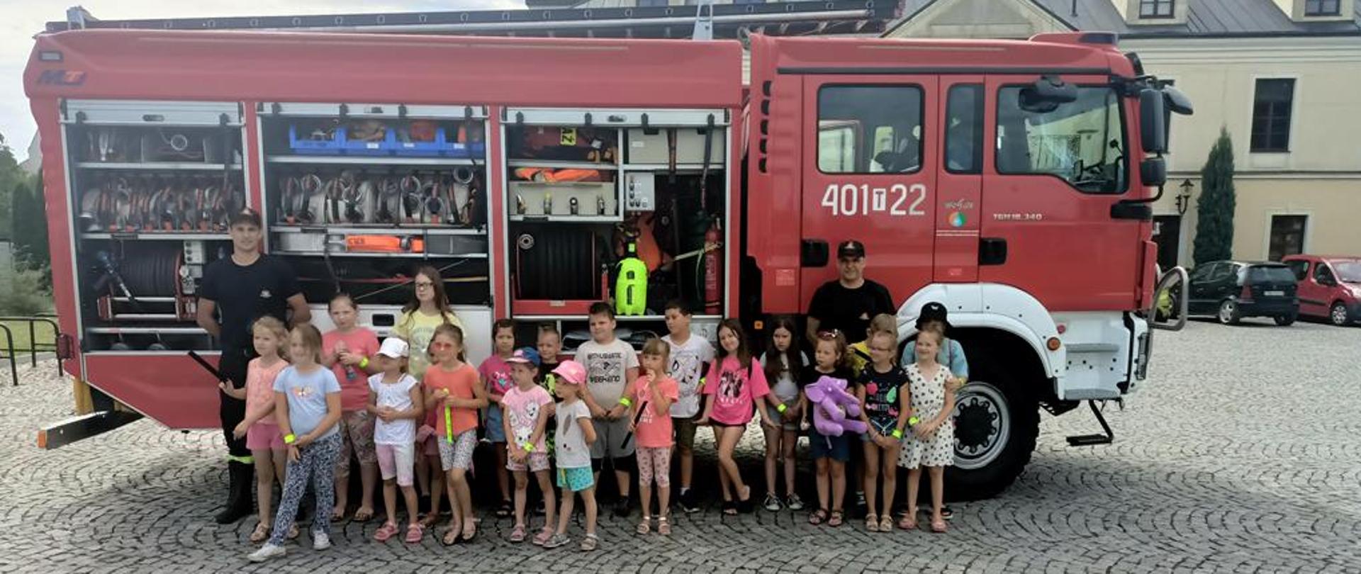 Zdjęcie przedstawia grupę młodzieży na tle czerwonego samochody gaśniczego.