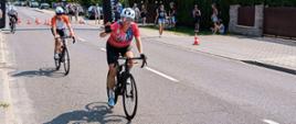 Zdjęcie przedstawia uczestników Mistrzostw Służb Mundurowych i Paramundurowych w ramach Garmin Triathlon Tour Rawa Mazowiecka 2026 podczas jazdy na rowerze, w tle wielki baner garmin i obserwujący ludzie