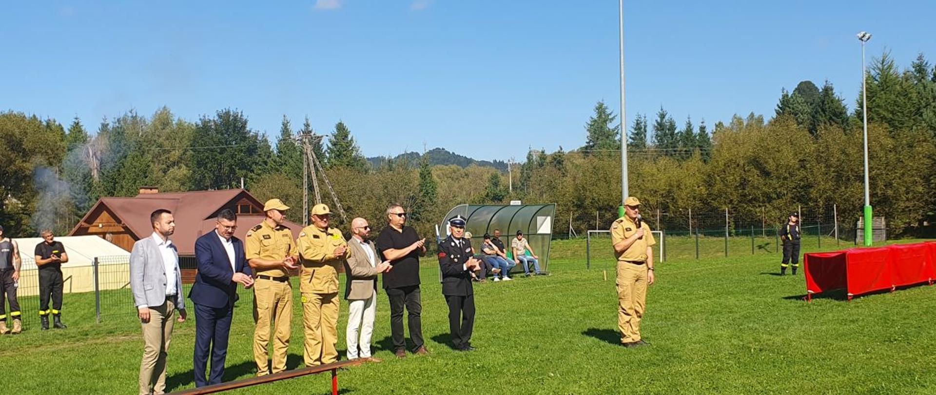 Zdjęcie przedstawia przemawiającego komendanta PSP oraz stojących obok: jego zastępcę, burmistrzów gminy Czarna i Lutowiska, burmistrza Ustrzyk Dolnych, posła, kapelana oraz prezesa ZOSP. W tle ludzie postronni. 