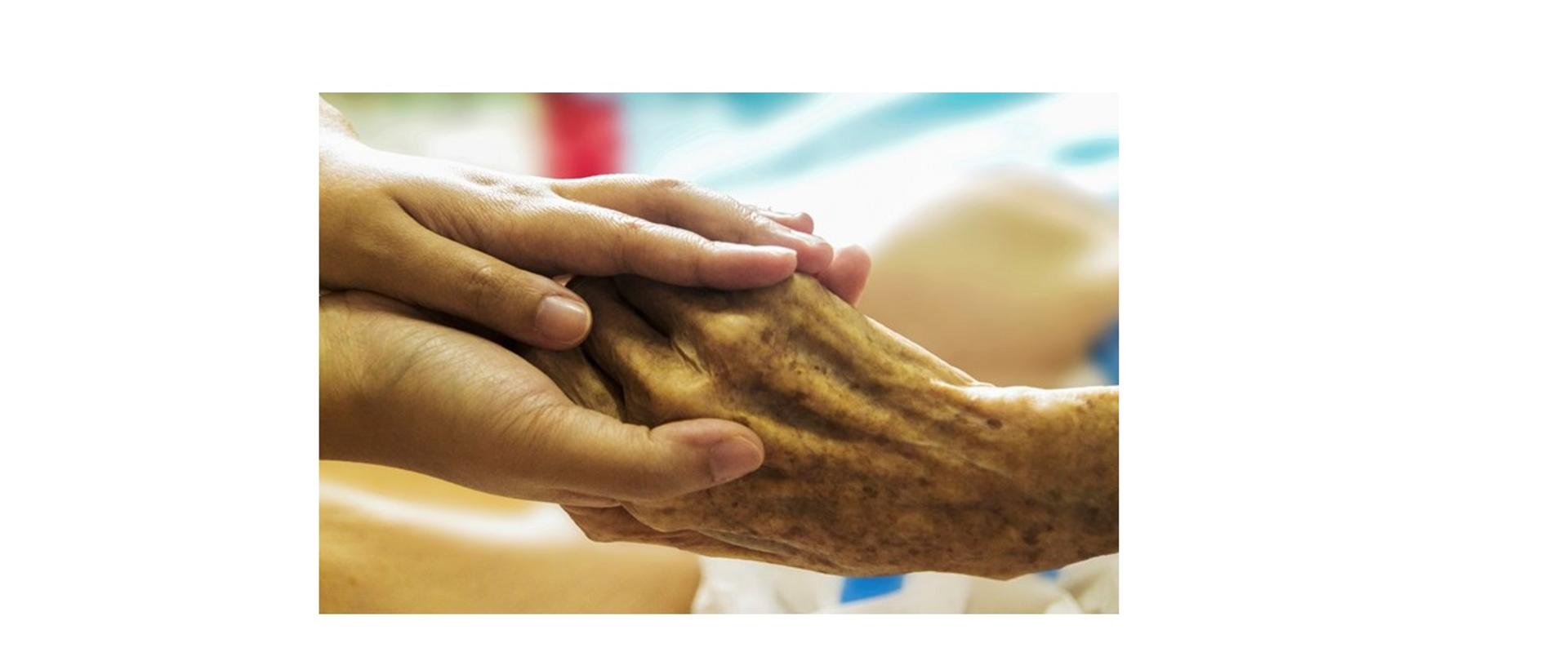 grafika przedstawia dłonie osoby młodszej obejmujące dłoń osoby starszej