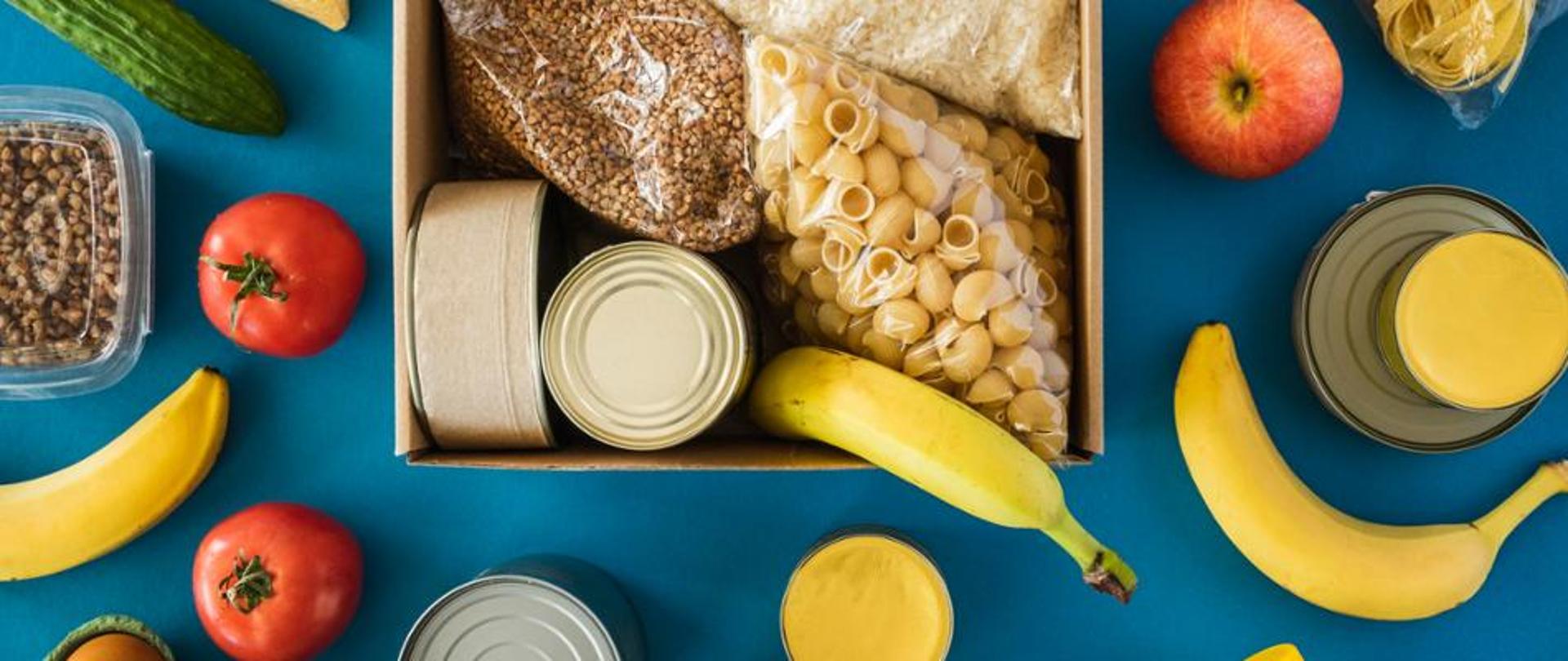 Na planszy widoczne różne produkty żywnościowe: makaron, kasza, banany, pomidory, konserwy