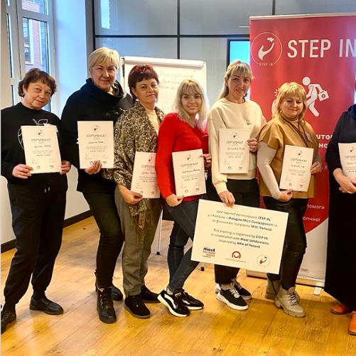 8 kobiet pozuje do zdjęcia z certyfikatami i planszą z informacją, że projekt został zrealizowany przez Step In, Most Solidarności z finansowaniem MFA of Poland