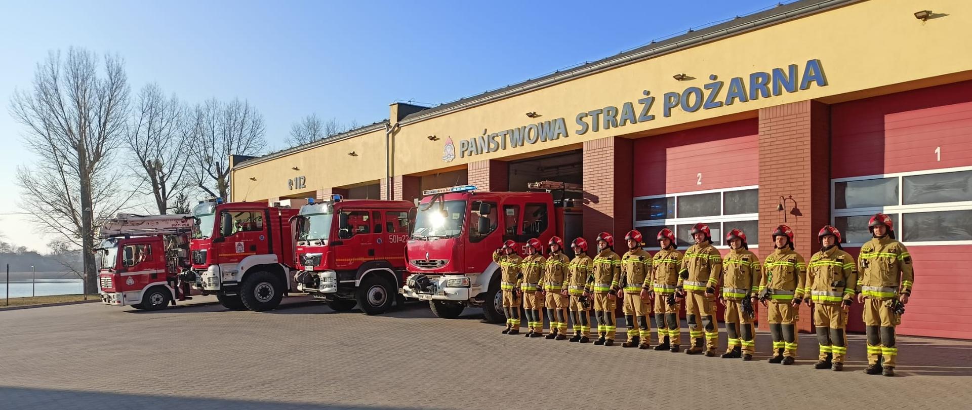 Na zdjęciu widzimy samochody pożarnicze oraz funkcjonariuszy KP PSP w Międzychodzie stojących w szeregu przed garażami wyjazdowymi w trakcie minuty ciszy dla poległych strażaków z Ukrainy