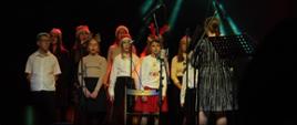 Zdjęcie przedstawia chór PSM I stopnia w Jarocinie wraz z nauczyciel Karoliną Skrzypczyńską podczas występu na koncercie świątecznym.