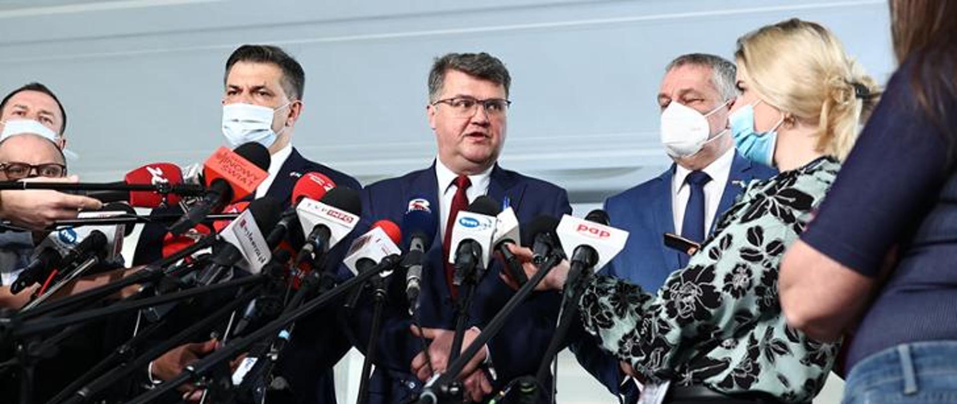 6 osób stojących przed kilkunastoma mikrofonami