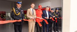 Na zdjęciu widzimy Zastępcę Komendanta Wojewódzkiego Państwowej Straży Pożarnej w Rzeszowie, który wraz z oficjelami dokonuje przecięcia wstęgi nowo rozbudowanego budynku remizy Ochotniczej Straży Pożarnej.