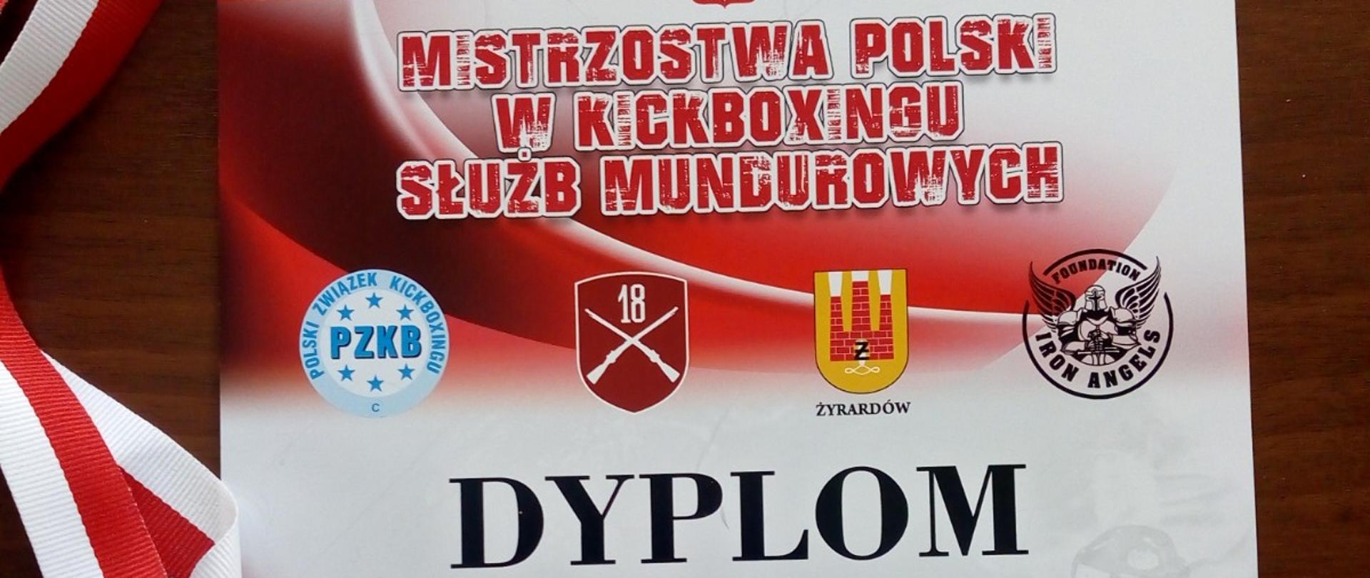 Zdjęcie przedstawia pamiątkowy dyplom oraz brązowy medal za zajęcie III miejsca w mistrzostwach polski w kickboxingu służb mundurowych. Medal w kształcie trapezu w kolorze brązowym. U góry do medalu przypięta jest biało – czerwona wstążka służąca do zakładania medalu na szyję zawodnikowi podczas ceremonii dekoracji. Dyplom w kolorze czerwono – białym patrząc od góry. Na dyplomie widnieje napis (od góry): mistrzostwa polski w kickboxingu służb mundurowych, poniżej umieszczone są loga partnerów oraz znajduje się napis: dyplom dla szymona grabowskiego za zajęcie trzeciego miejsca na mistrzostwach polski służb mundurowych. Poniżej określona jest kategoria wagowa do 89 kg. Na samym dole: Żyrardów, 23 - 25 września 2022 r. 