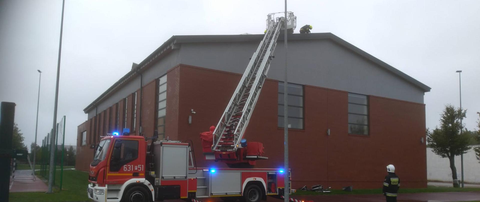Na zdjęciu widać wóz strażacki oraz strażaków pracujących na dachu 