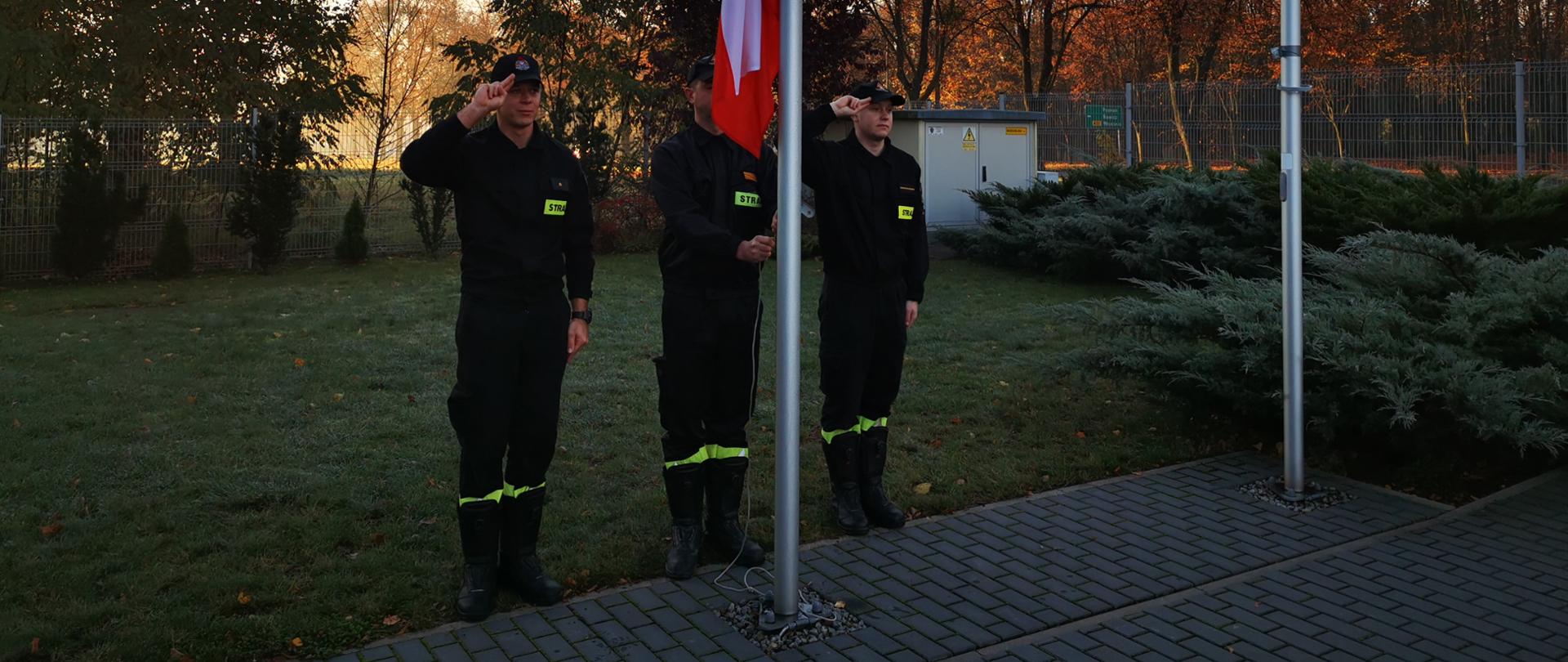 Na zdjęciu poczet flagowy przy maszcie 3 strażaków podczas wciągania flagi na maszt 