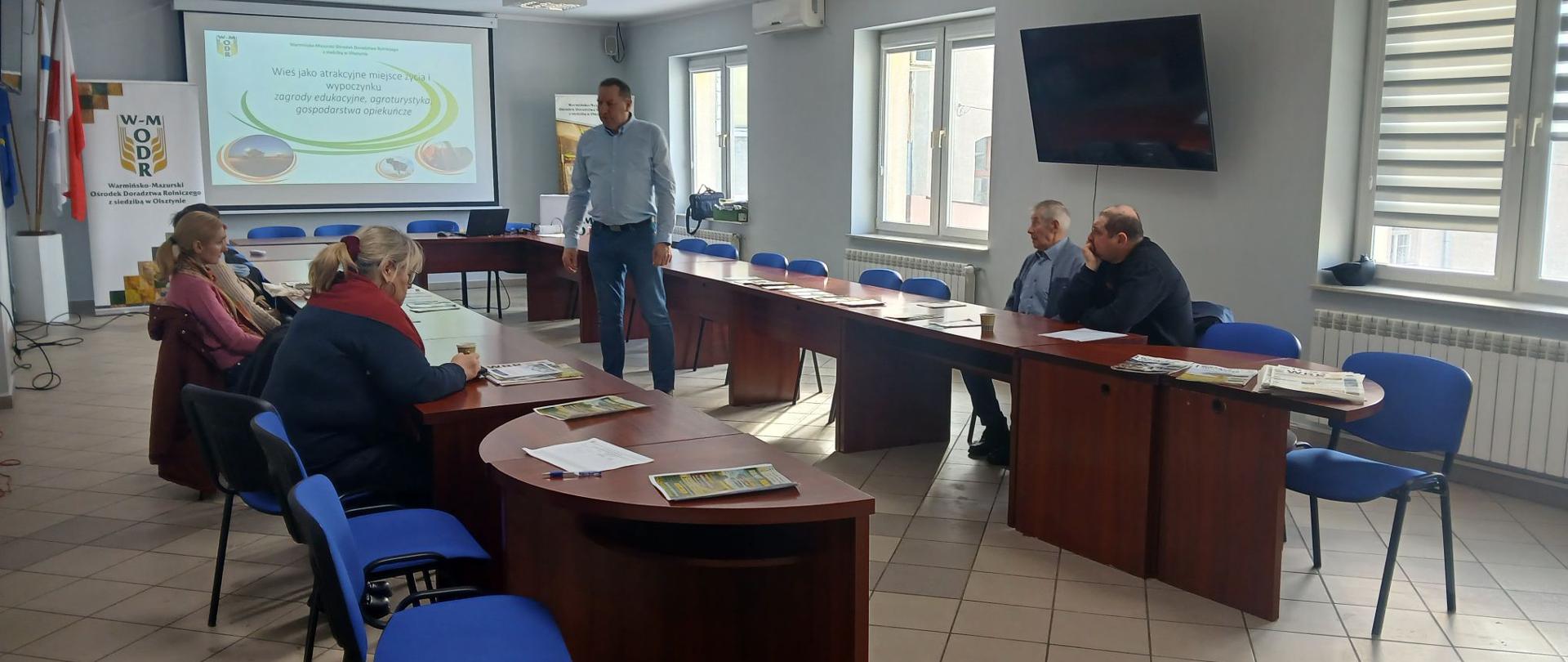 Grupa osób siedzi przy stole i słucha wykładu