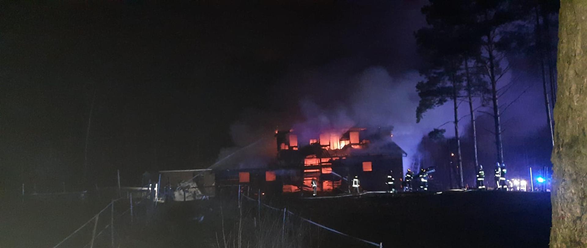 Wykonane jest po zmroku. Ze znacznej odległości widać że pożar został już zlokalizowany. Przed zniszczonym budynkiem widać strażaków którzy dogaszają pożar i przystępują do prac rozbiórkowych. 