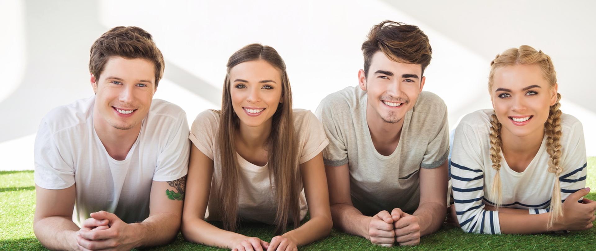 Młodzi i uśmiechnięci ludzie leżą na zielonej trawie