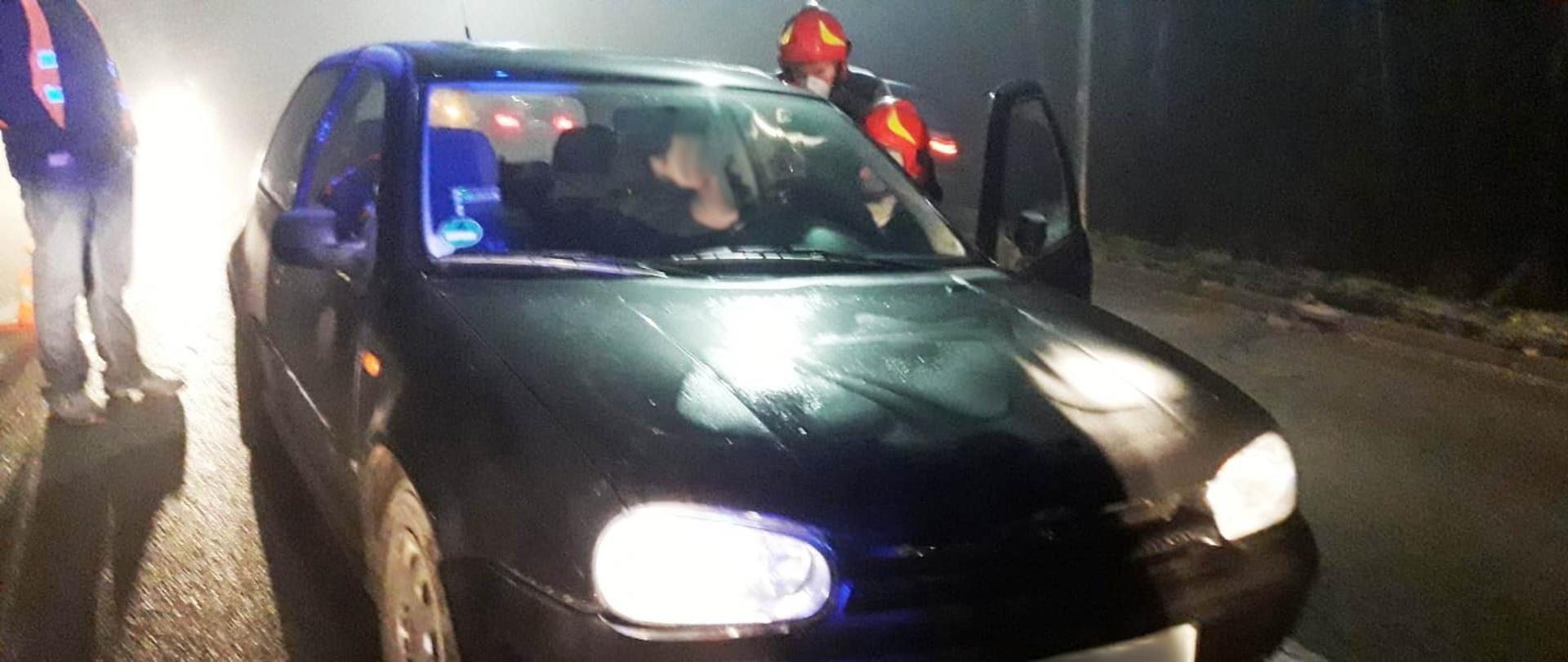 Samochód osobowy uczestniczący w zdarzeniu, w środku kierująca z którą rozmawia dwóch strażaków.