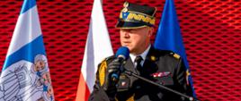 Zdjęcie przedstawia Wielkopolskiego Komendanta Wojewódzkiego Państwowej Straży Pożarnej nadbrygadiera Dariusza Matczaka, który stoi przy mównicy i przemawia. 