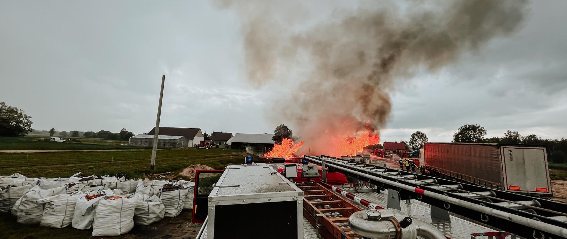 Zdjęcie wykonane z wozu strażackiego pożaru palet. W pobliżu zagrożone samochody i worki z pelletem