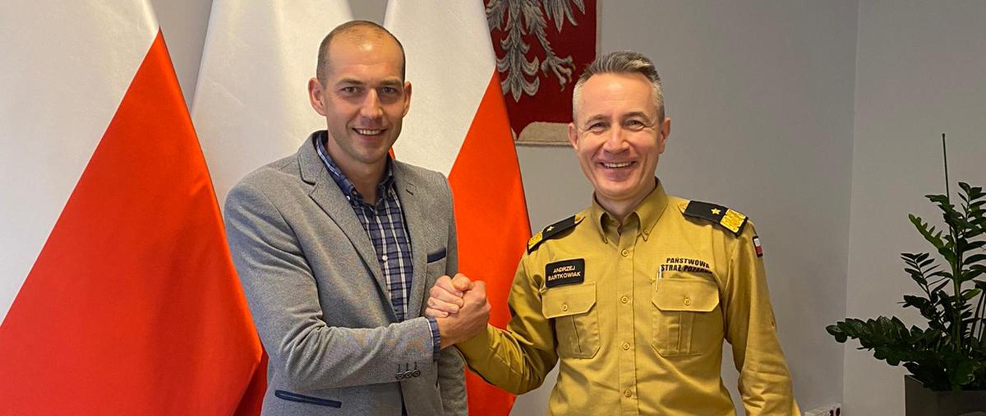 Komendant Główny PSP w uścisku ręki z kpt. Bródką pozują do zdjęcia, w tle 3 flagi RP oraz godło na ścianie