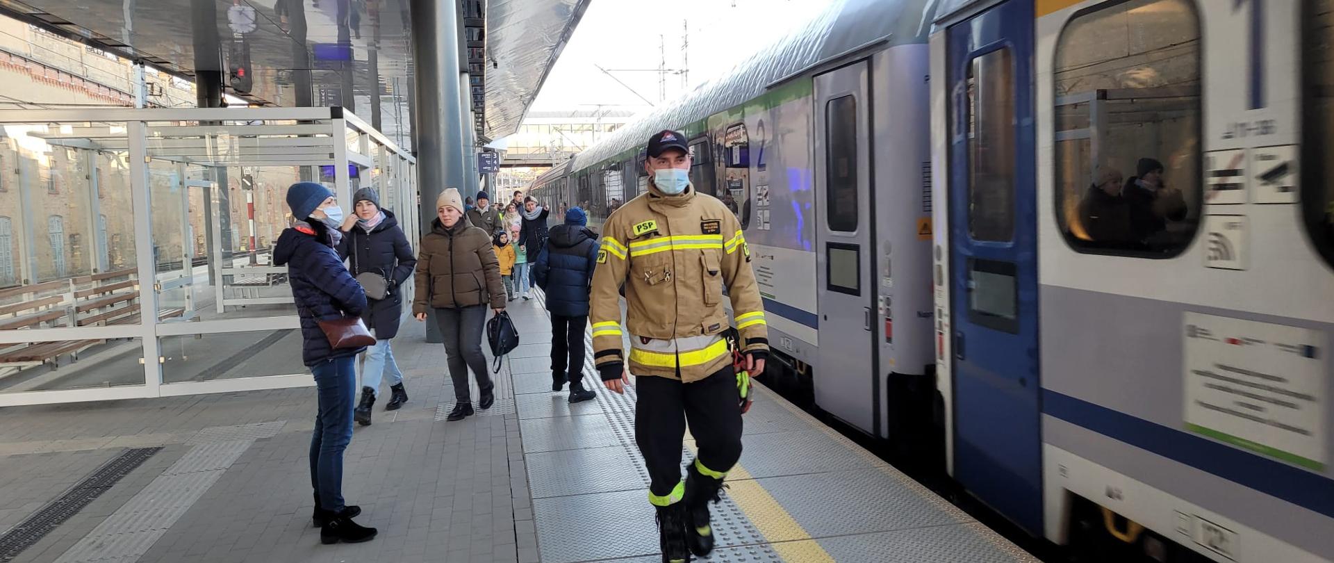 Strażak Państwowej Straży Pożarnej koordynujący przyjazd uchodźców na peronie PKP
