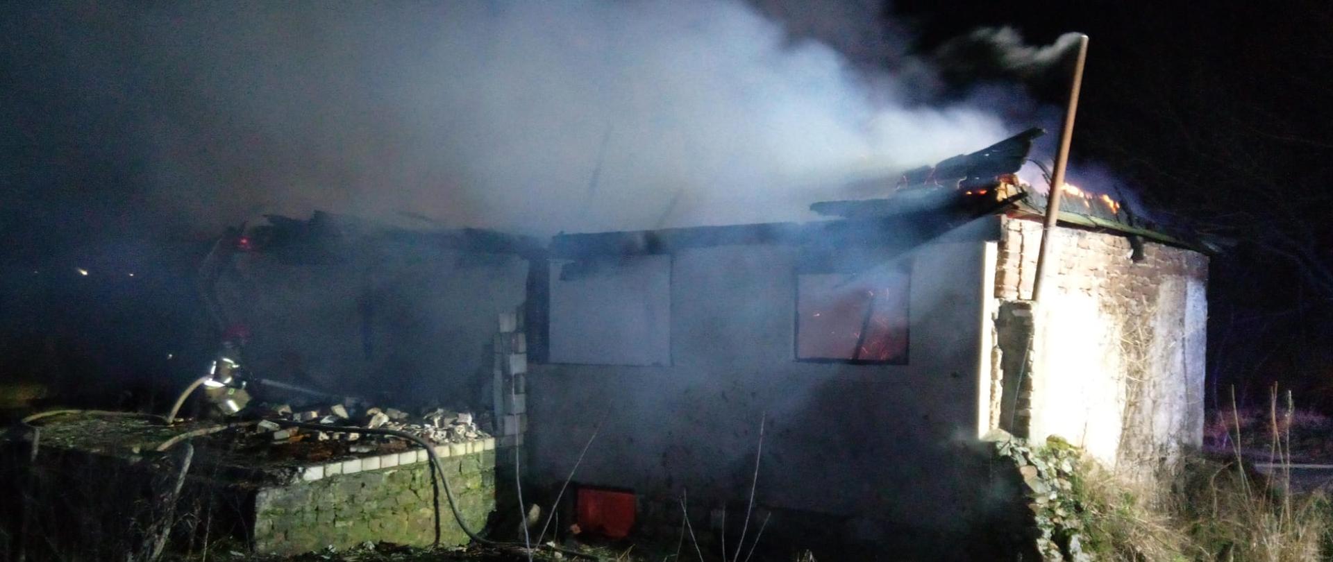 Zdjęcie przedstawia stary młyn, który uległ spaleniu. Nad budynkiem unosi się dym i para wodna. 