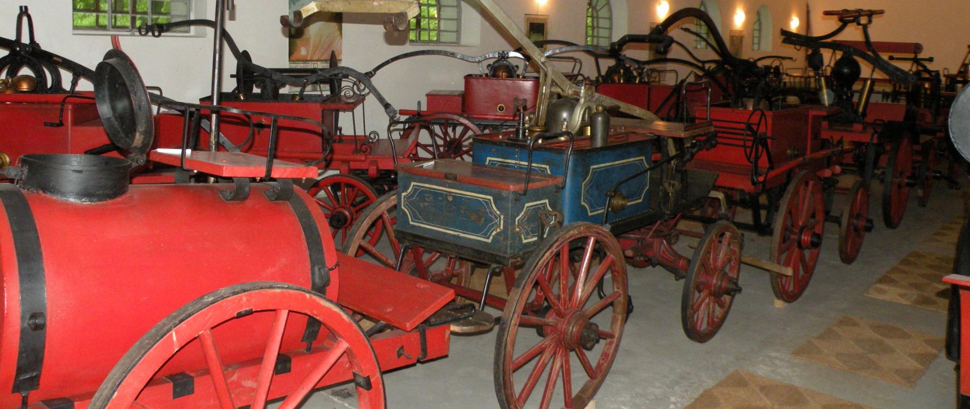 Zdjęcie przedstawia wnętrze jednej z sal wystawowych na którym znajdują się dawne powozy konne służące do gaszenia pożarów 