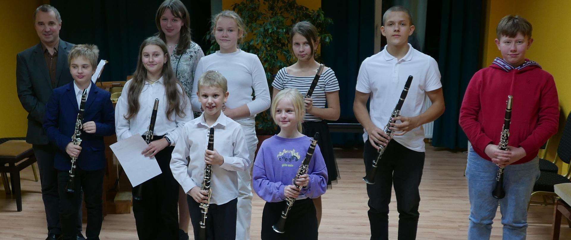 grupowe zdjęcie uczniów z klarnetami r rękach. Po lewej stronie stoi razem z nimi nauczyciel