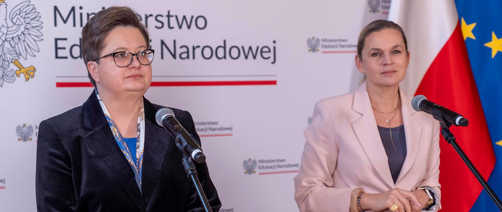 Zdjęcie przedstawia Minister Edukacji Barbarę Nowacką wraz z Sekretarzem stanu Katarzyną Lubnauer, które stoją przed mikrofonami. 