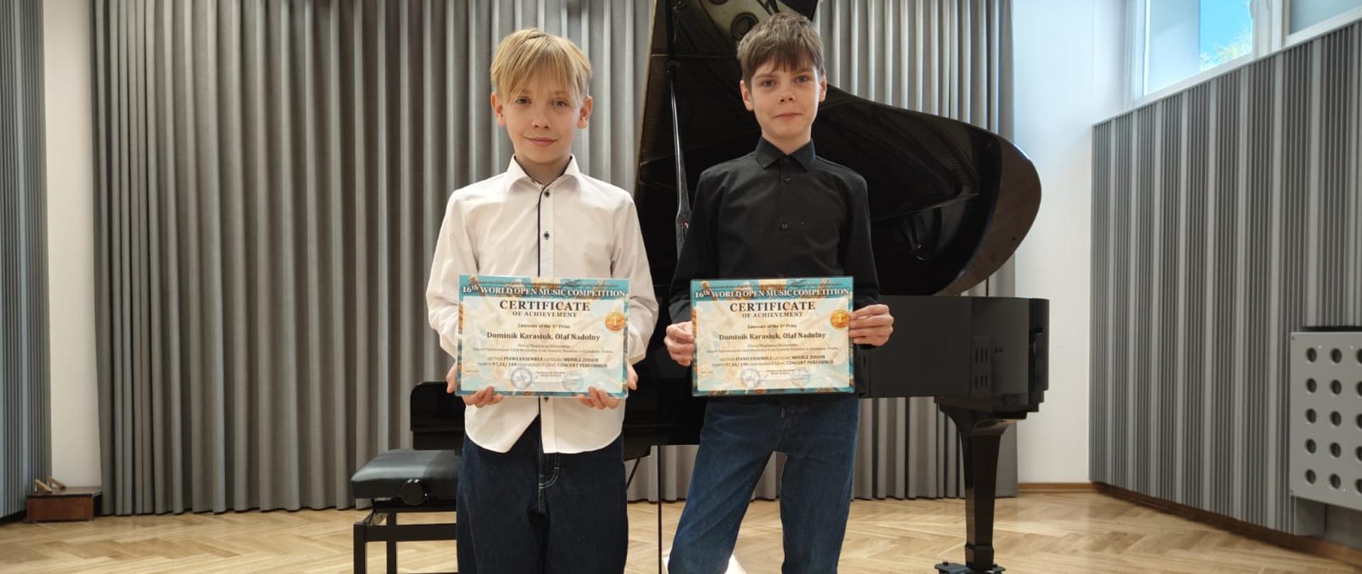 Uczniowie stoją z dyplomami na tle fortepianu