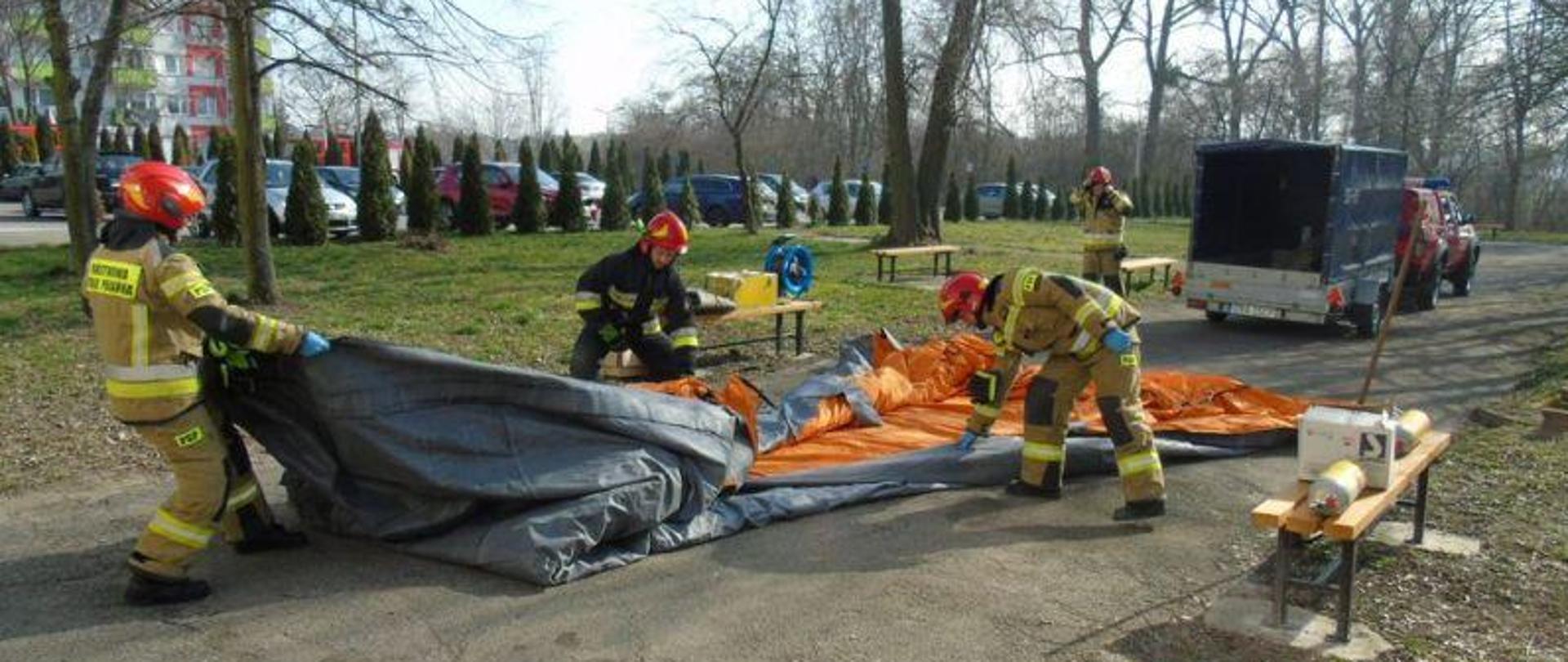 Zdjęcie strażaków w trakcie ćwiczeń z zakresu zagrożenia epidemiologicznego. Strażacy rozkładają namiot pneumatyczny.