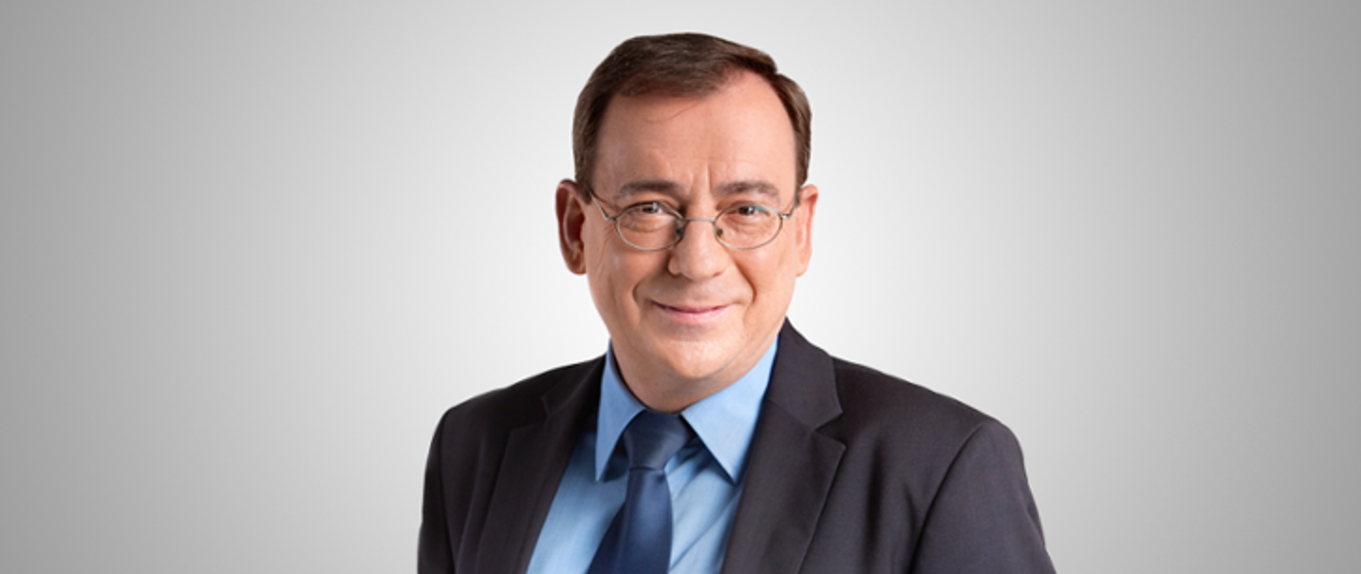 Zdjęcie przedstawia Ministra Spraw Wewnętrznych i Administracji. Zdjęcie wykonane na szarym tle.