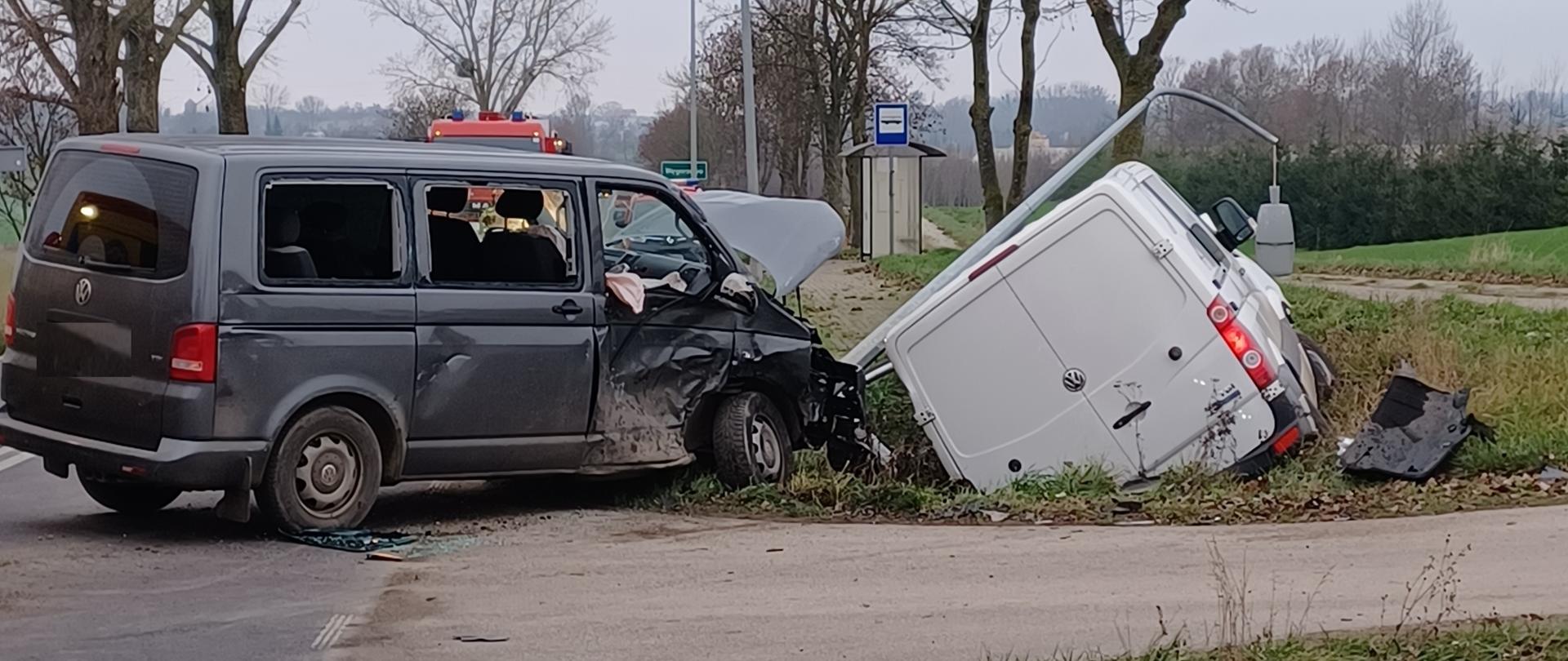 Zderzenie dwóch busów. Jeden z nich stoi na drodze i ma rozbity prawy bok, drugi znajduje się w rowie i ma rozbity przód. 