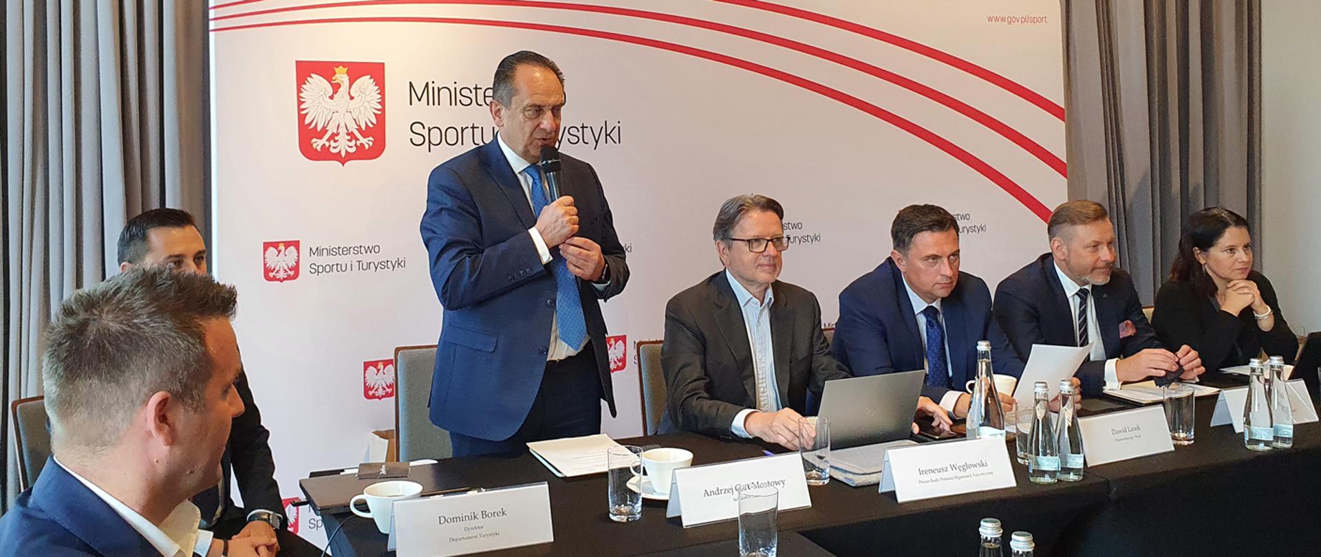 Wspólne posiedzenie Rady POT i Rady Ekspertów ds. Turystyki, Gdańsk 15.07.2022. Uczestnicy spotkania siedzą przy stole. Z mikrofonem stoi minister Andrzej Gut-Mostowy.