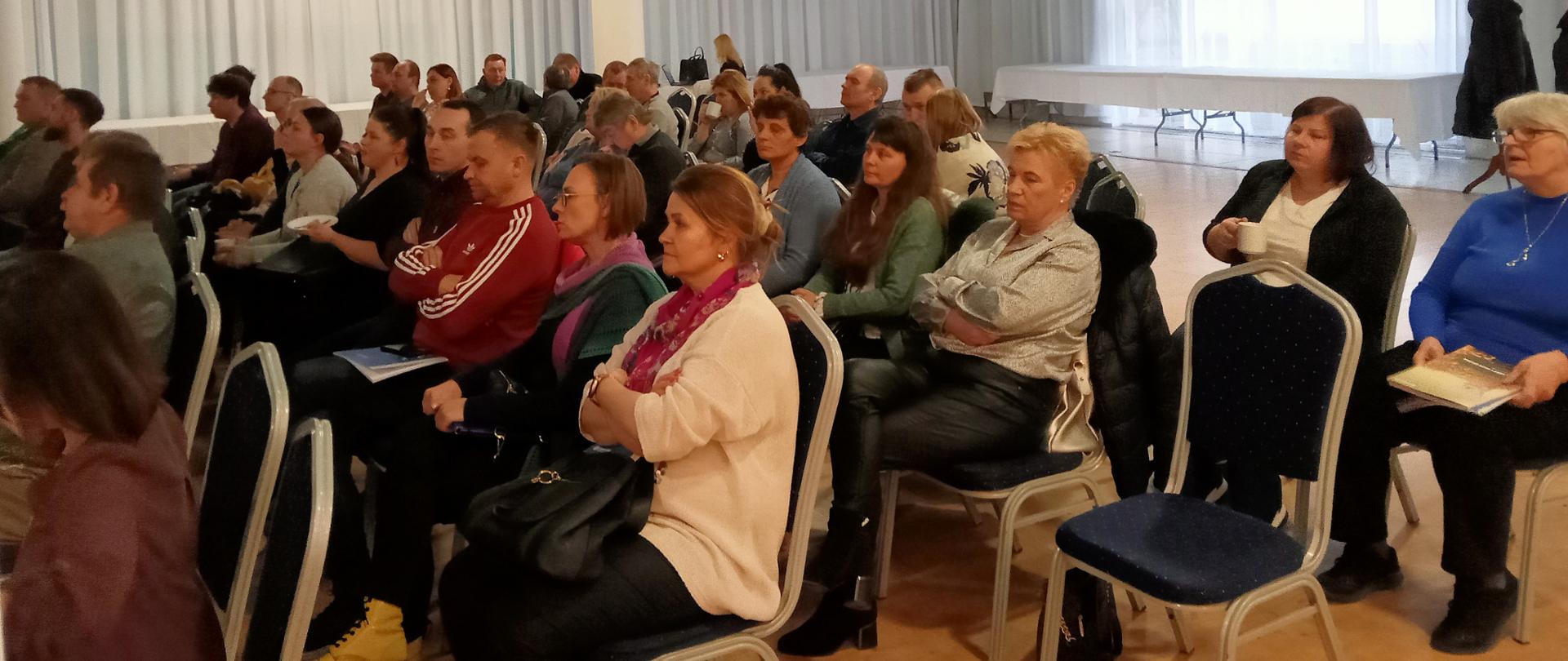 Uczestnicy spotkania słuchają wykładu siedząc na krzesłach ułożonych w kilku rzędach 