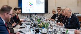 Grupa osób siedzi przy stole konferencyjnym, z tyłu wyświetla się prezentacja z napisem Aktualizacja Wieloletniego programu współpracy rozwojowej 2021-2030. Solidarność dla rozwoju