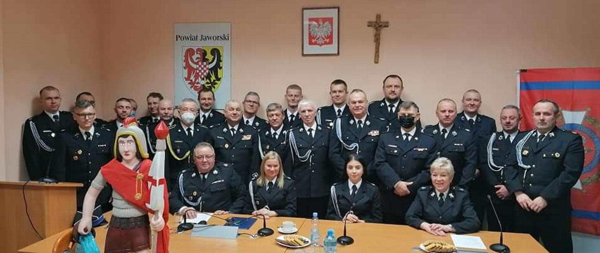 Obraz przedstawia strażaków z terenu powiatu jaworskiego podczas zjazdu powiatowego. Strażacy w umundurowaniu wyjściowym. Osoby znajdują się w pomieszczeniu.