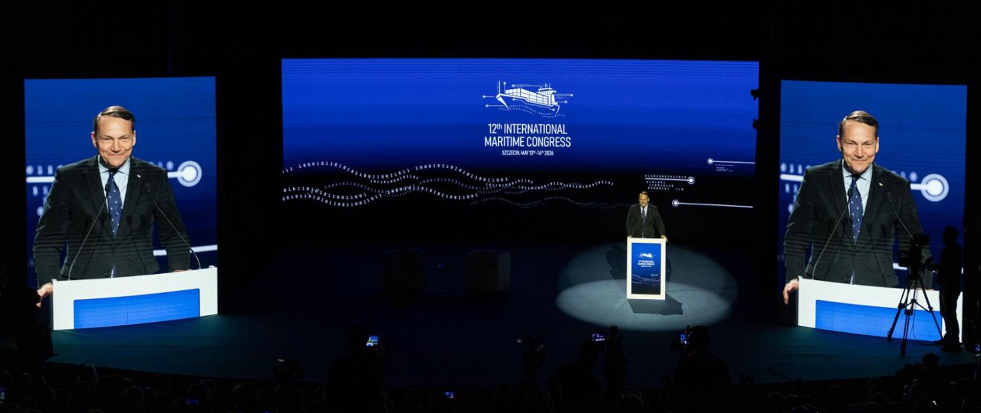 The photo shows a man in a suit standing at the lectern. Behind him is a sign that reads "12th International Maritime Congress"