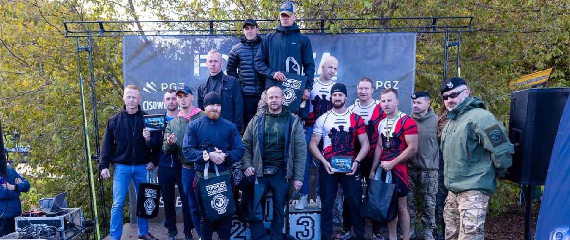 Zdjęcie przedstawia uczestników wydarzenia, stojących na podium