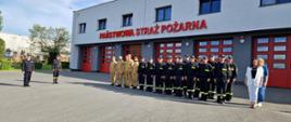 Strażacy oraz pracownicy komendy stoją w szyku na uroczystej zbiórce z okazji święta flagi na tle budynku komendy