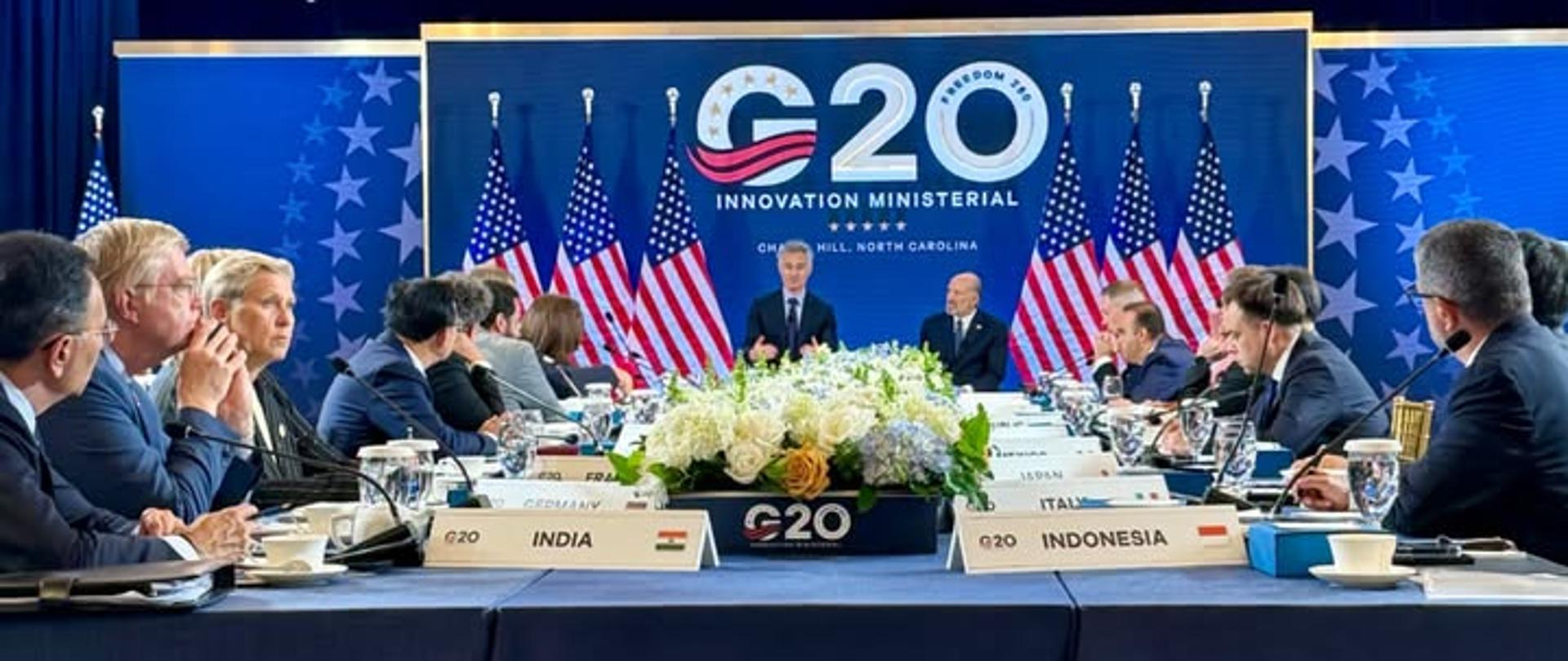 Reprezentanci krajów siedzący przy stole konferencyjnym. W tle Granatowa ścianka z logo amerykańskiej prezydencji G20 i sześcioma amerykańskimi flagami.