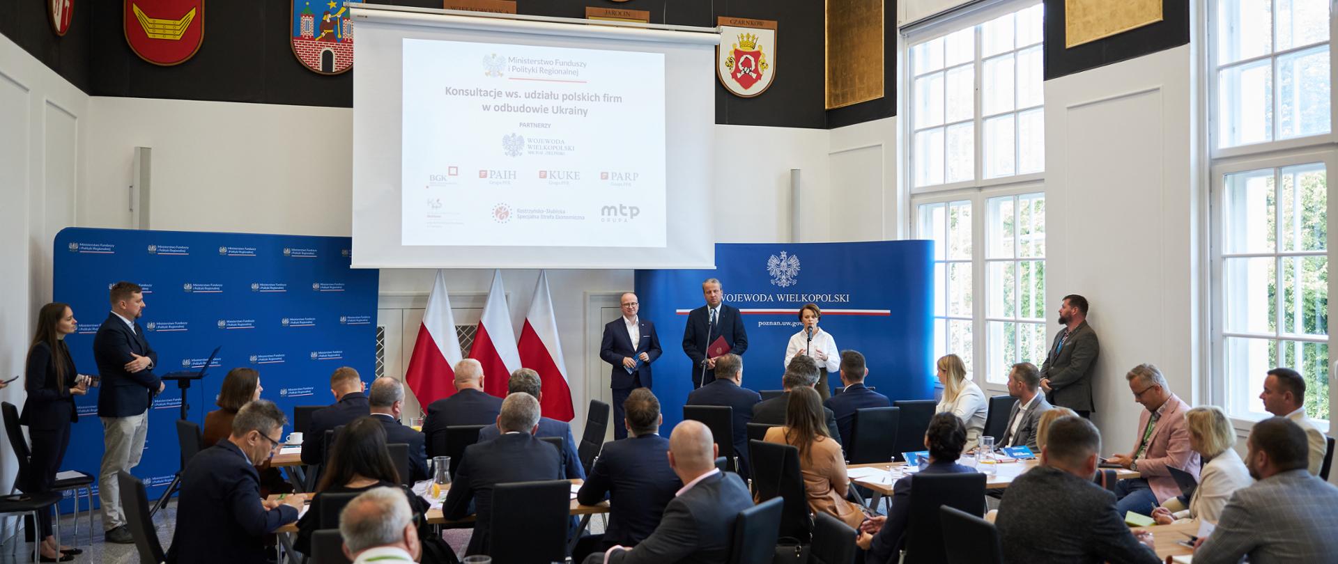 Grupa osób stoi i siedzi na dużej sali